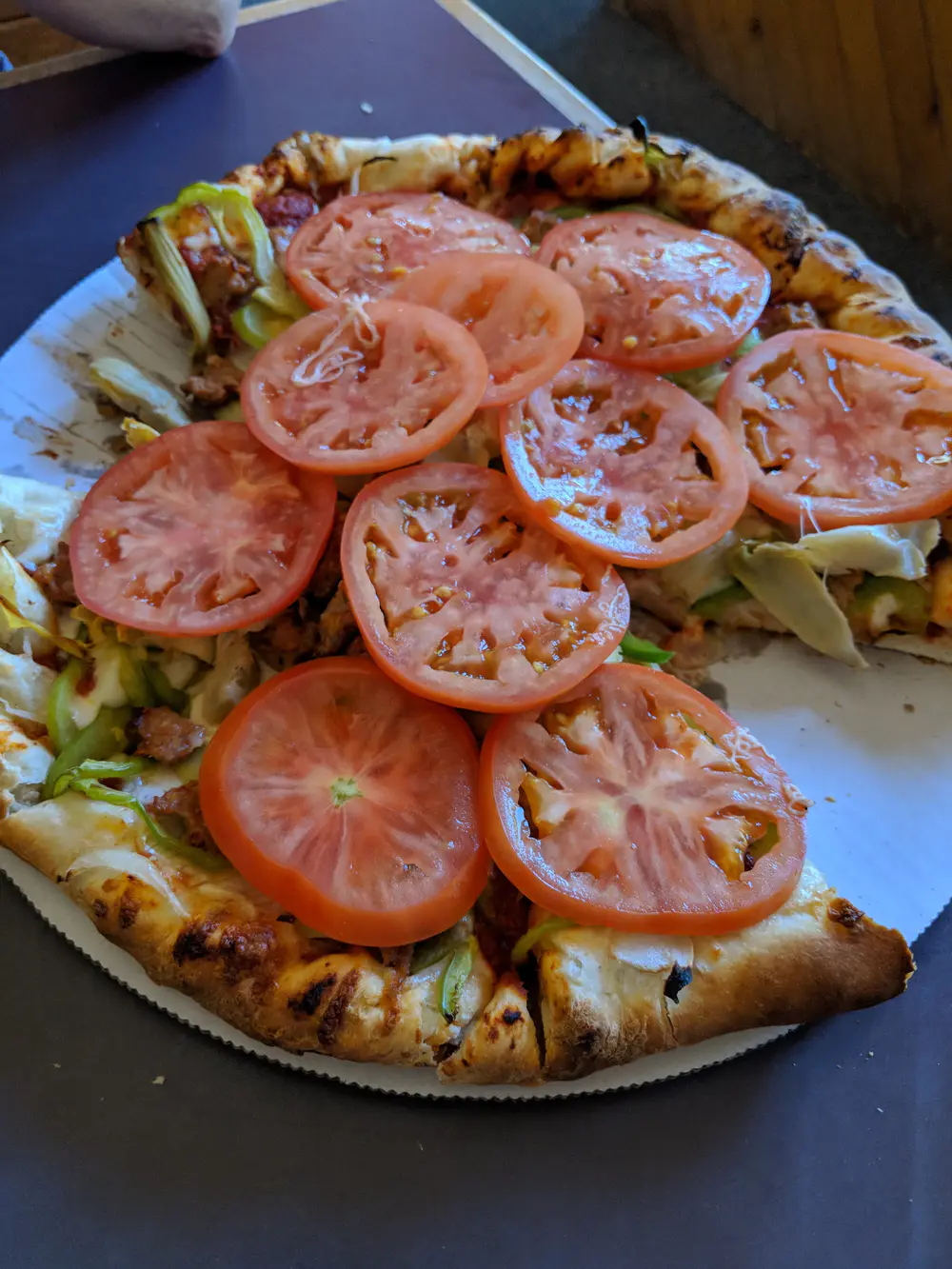 A Woodstock's pizza piled with sliced tomatoes, artichoke and green peppers